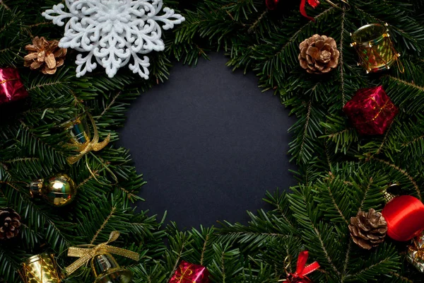 Christmas wreath decorated with a white snowflake, cones, red ball, red snowflake and beads on a black background