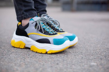 Spor ayakkabılı ayaklar asfalt yolda, çok renkli sarı, beyaz, siyah ve mavi. Yakın plan.