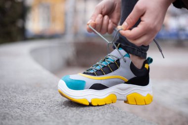 # Sarı, beyaz, siyah ve mavi ayakkabı bağcıkları bağlayan kız #