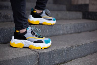 Mermer merdivenlerde çok renkli, sarı, beyaz, siyah ve mavi spor ayakkabılı ayaklar.