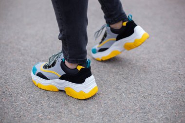 Spor ayakkabılı ayaklar asfalt yolda, çok renkli sarı, beyaz, siyah ve mavi. Yakın plan.