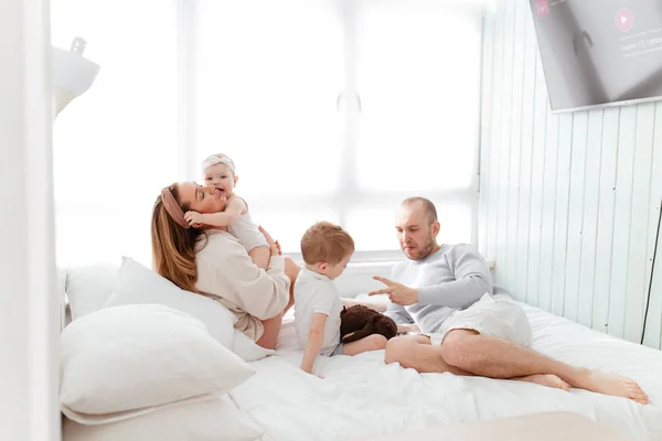 Genç, mutlu bir aile ve küçük çocuklar, yatakta uzanıyorlar, sarılıyorlar, ev kıyafetleriyle gülüyorlar, rahat bir evde, anne, baba, oğul ve kız