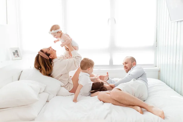 Genç, mutlu bir aile ve küçük çocuklar, yatakta uzanıyorlar, sarılıyorlar, ev kıyafetleriyle gülüyorlar, rahat bir evde, anne, baba, oğul ve kız