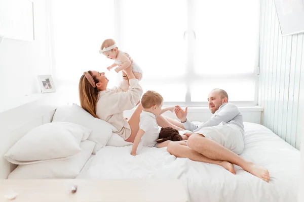 Genç, mutlu bir aile ve küçük çocuklar, yatakta uzanıyorlar, sarılıyorlar, ev kıyafetleriyle gülüyorlar, rahat bir evde, anne, baba, oğul ve kız