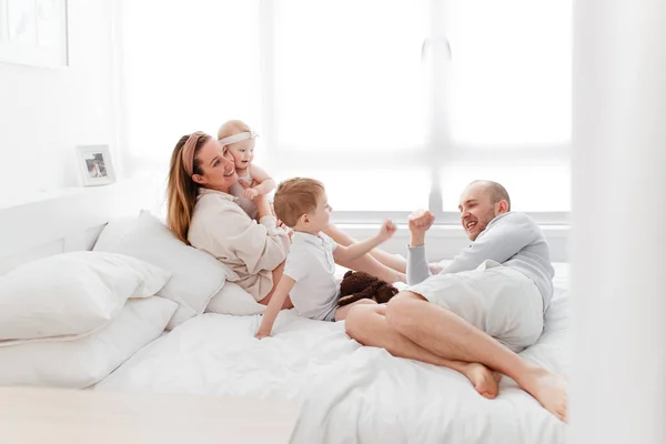 Genç, mutlu bir aile ve küçük çocuklar, yatakta uzanıyorlar, sarılıyorlar, ev kıyafetleriyle gülüyorlar, rahat bir evde, anne, baba, oğul ve kız