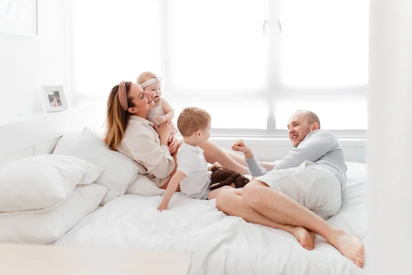 Genç, mutlu bir aile ve küçük çocuklar, yatakta uzanıyorlar, sarılıyorlar, ev kıyafetleriyle gülüyorlar, rahat bir evde, anne, baba, oğul ve kız
