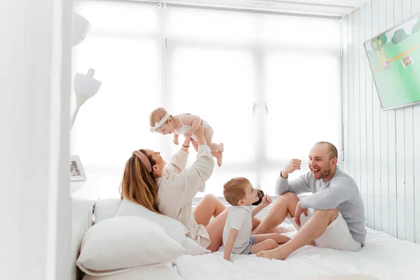 Genç, mutlu bir aile ve küçük çocuklar, yatakta uzanıyorlar, sarılıyorlar, ev kıyafetleriyle gülüyorlar, rahat bir evde, anne, baba, oğul ve kız