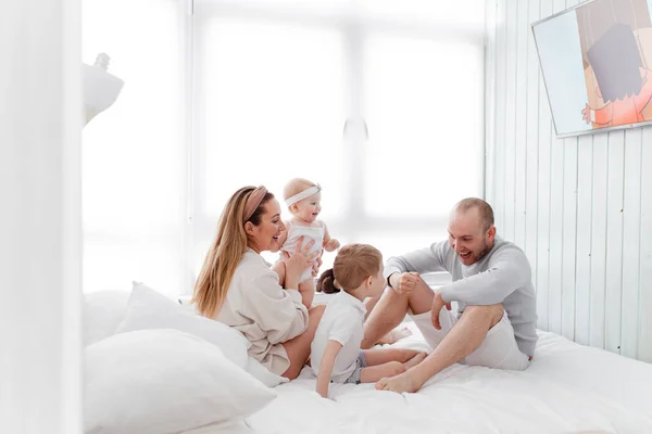 Genç, mutlu bir aile ve küçük çocuklar, yatakta uzanıyorlar, sarılıyorlar, ev kıyafetleriyle gülüyorlar, rahat bir evde, anne, baba, oğul ve kız