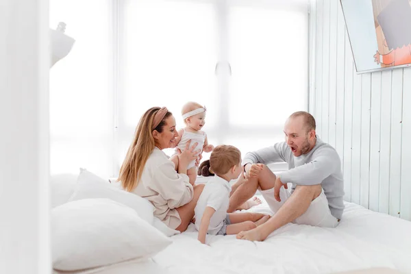 Genç, mutlu bir aile ve küçük çocuklar, yatakta uzanıyorlar, sarılıyorlar, ev kıyafetleriyle gülüyorlar, rahat bir evde, anne, baba, oğul ve kız