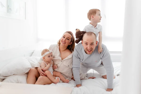 Genç, mutlu bir aile ve küçük çocuklar, yatakta uzanıyorlar, sarılıyorlar, ev kıyafetleriyle gülüyorlar, rahat bir evde, anne, baba, oğul ve kız