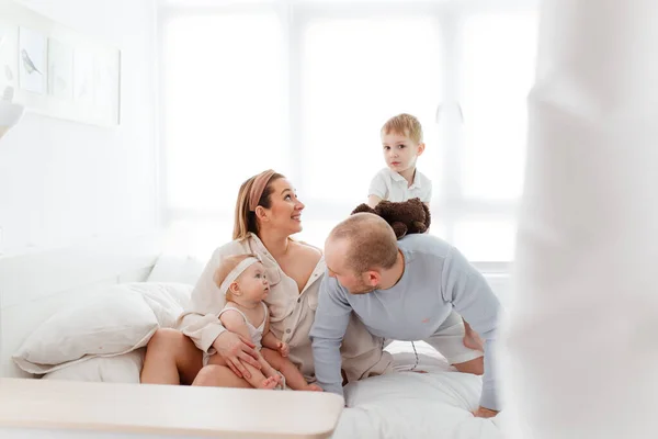 Genç, mutlu bir aile ve küçük çocuklar, yatakta uzanıyorlar, sarılıyorlar, ev kıyafetleriyle gülüyorlar, rahat bir evde, anne, baba, oğul ve kız