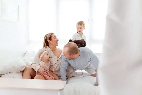 Genç, mutlu bir aile ve küçük çocuklar, yatakta uzanıyorlar, sarılıyorlar, ev kıyafetleriyle gülüyorlar, rahat bir evde, anne, baba, oğul ve kız