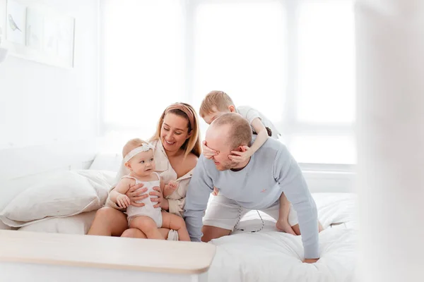 Genç, mutlu bir aile ve küçük çocuklar, yatakta uzanıyorlar, sarılıyorlar, ev kıyafetleriyle gülüyorlar, rahat bir evde, anne, baba, oğul ve kız