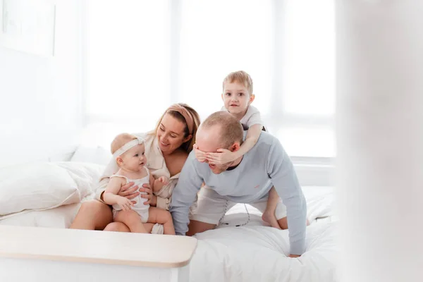 Genç, mutlu bir aile ve küçük çocuklar, yatakta uzanıyorlar, sarılıyorlar, ev kıyafetleriyle gülüyorlar, rahat bir evde, anne, baba, oğul ve kız