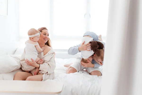Genç, mutlu bir aile ve küçük çocuklar, yatakta uzanıyorlar, sarılıyorlar, ev kıyafetleriyle gülüyorlar, rahat bir evde, anne, baba, oğul ve kız