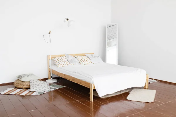 The interior of the bedroom. A spacious, bright, fresh bedroom with white walls and wooden floor, with a decor of small rugs, wicker seat and floor lamp