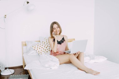 Pembe pijamalı, dizüstü bilgisayarlı, evde, internette, iş yerinde, yatakta uzanan, telefonla konuşan, sipariş, dükkan, parlak iç mekan.