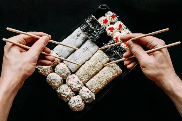 Japon yemek servisi elinde çubuklarla siyah bir arka planda plastik bir kutuda yuvarlanıyor.