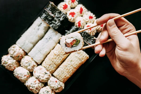 Japon yemek servisi elinde çubuklarla siyah bir arka planda plastik bir kutuda yuvarlanıyor.