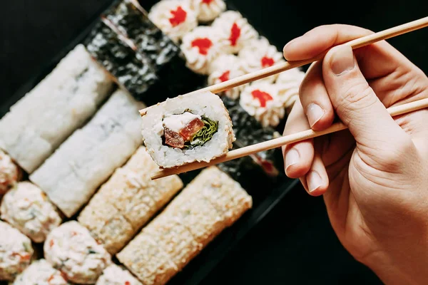 Japon yemek servisi elinde çubuklarla siyah bir arka planda plastik bir kutuda yuvarlanıyor.