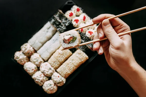 Japon yemek servisi elinde çubuklarla siyah bir arka planda plastik bir kutuda yuvarlanıyor.