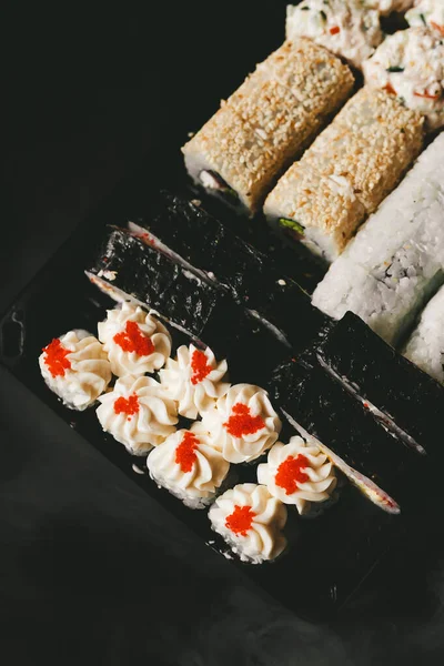 Japon yemek servisi elinde çubuklarla siyah bir arka planda plastik bir kutuda yuvarlanıyor.