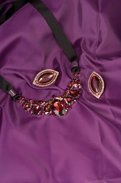Purple glass necklace and earrings on textile background