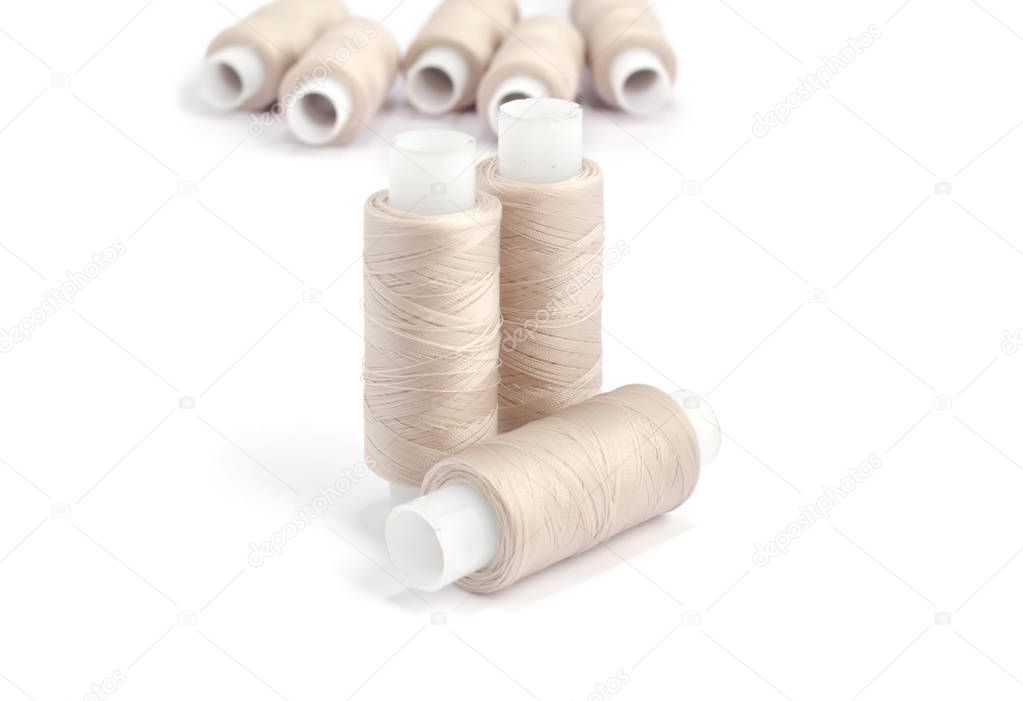 Spools of beige cotton threads on white background