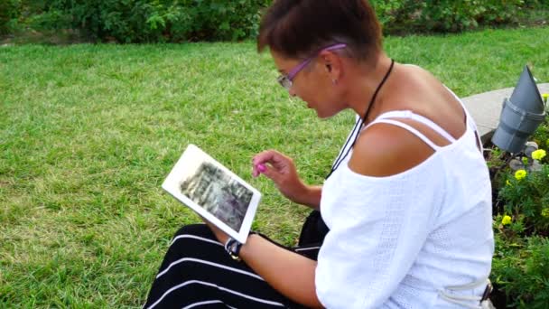 Junge Frau mit Tablet-Computer sitzt im Stadtpark — Stockvideo