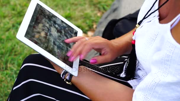 Молода жінка з планшетним комп'ютером сидить у міському парку — стокове відео
