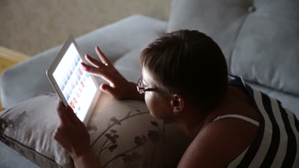 Junge Frau blättert Fotos auf Tablet-Computer liegend auf Sofa zu Hause — Stockvideo