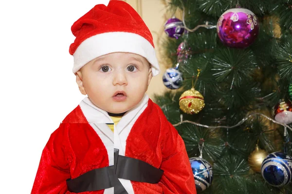 Sehr niedlicher kaukasischer kleiner Junge im Weihnachtsmannkostüm mit Weihnachtsbaum und Dekoration im Hintergrund. Junge schaut in die Kamera. Weihnachtskonzept — Stockfoto