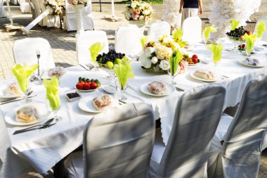 Elegant banquet tables prepared for a conference or a party and covered with a white tablecloth and decorated with flowers for guests.