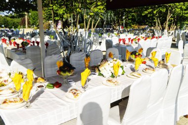 Elegant banquet tables prepared for a conference or a party and covered with a white tablecloth and decorated with flowers for guests.
