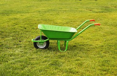 A green iron empty trash cart stands on the green grass,city services.