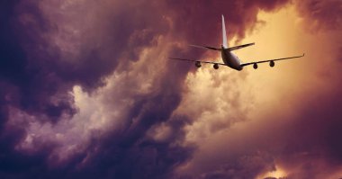 Airplane flying above dramatic clouds during sunset,sunrise.