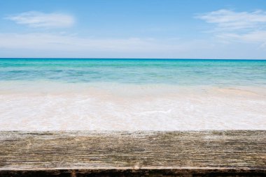 Tropik bir yaz plajına karşı kahverengi ahşap bir masa ve mavi gökyüzüne karşı bir deniz dalgası..