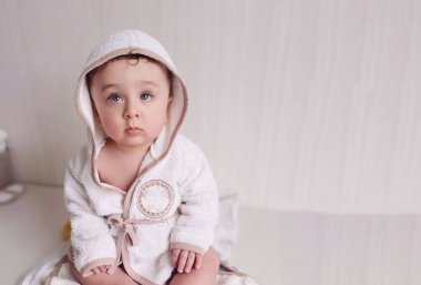 Bornozlu, sarı saçlı ve gözlü küçük bir çocuk masada oturuyor.