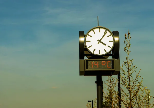 Круглые часы на открытом воздухе с электронным термометром на фоне голубого неба. — стоковое фото