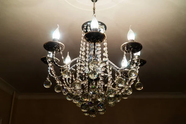 A crystal chandelier with light bulbs hangs from the ceiling. — Stock Photo, Image