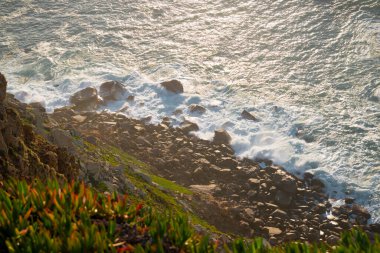 Dalgalar, uçurumlar ve kayalar Portekiz Cabo da Roca 'da batan güneş ışınlarında.