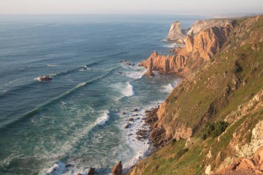 Dalgalar, uçurumlar ve kayalar Portekiz Cabo da Roca 'da batan güneş ışınlarında.