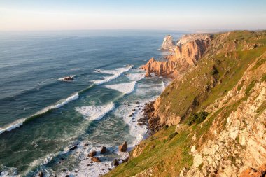 Dalgalar, uçurumlar ve kayalar Portekiz Cabo da Roca 'da batan güneş ışınlarında.