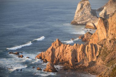 Dalgalar, uçurumlar ve kayalar Portekiz Cabo da Roca 'da batan güneş ışınlarında.