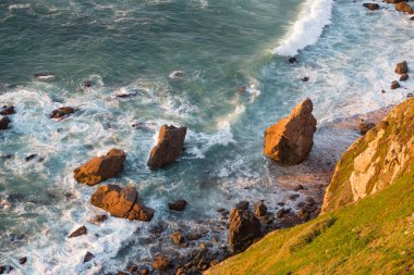 Dalgalar, uçurumlar ve kayalar Portekiz Cabo da Roca 'da batan güneş ışınlarında.