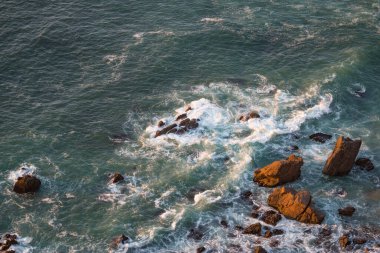 Dalgalar, uçurumlar ve kayalar Portekiz Cabo da Roca 'da batan güneş ışınlarında.