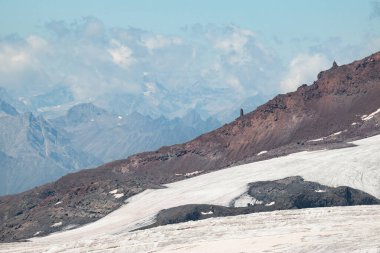 Elbrus yanardağının kırmızı yamacında beyaz buzullu, bulutlu ve Kafkasyalı gündüz dağları olan bir taş..