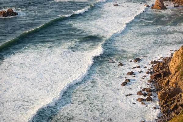 Dalgalar, uçurumlar ve kayalar Portekiz Cabo da Roca 'da batan güneş ışınlarında.