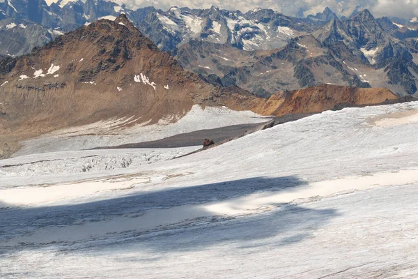 Elbrus yanardağının kırmızı yamacında beyaz buzullu, bulutlu ve Kafkasyalı gündüz dağları olan bir taş..