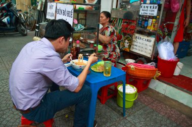Ho Chi Minh şehri, Vietnam - Aralık 2018: Vietnamlı adam sokaktaki küçük masadan şehriye yiyor..